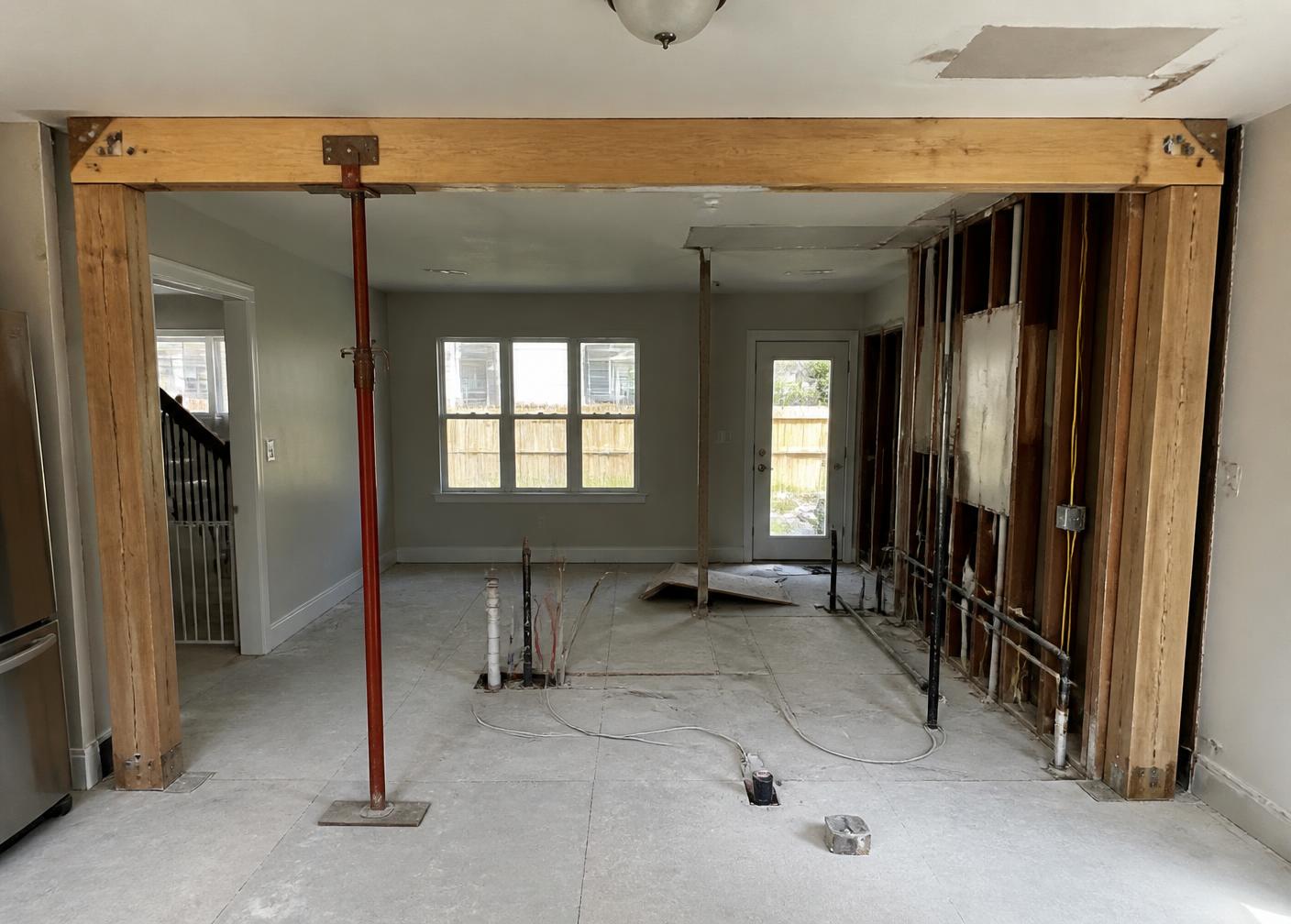 Kitchen wall removal in progress showing a structural beam, temporary shoring post, ceiling patch area, and exposed framing and utilities